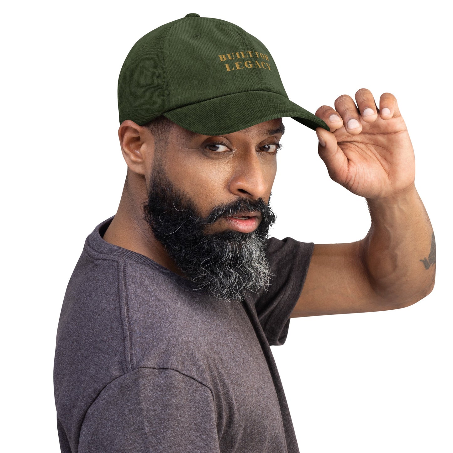 Dark olive corduroy heritage hat with “BUILT FOR LEGACY” embroidery, worn with raised hand