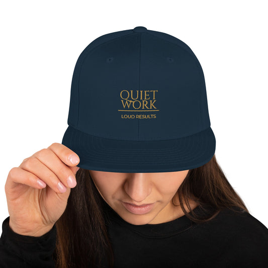 Dark navy snapback cap with "QUIET WORK" logo and "LOUD RESULTS"